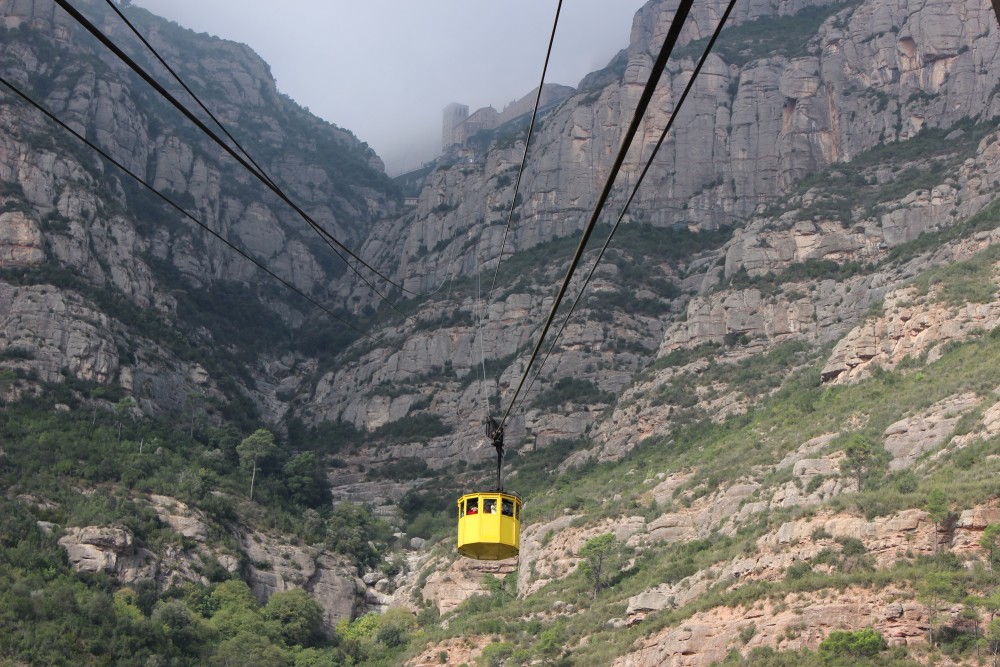 Bright yellow cable car heading to the Montserrat monastery at the top of the cliffs