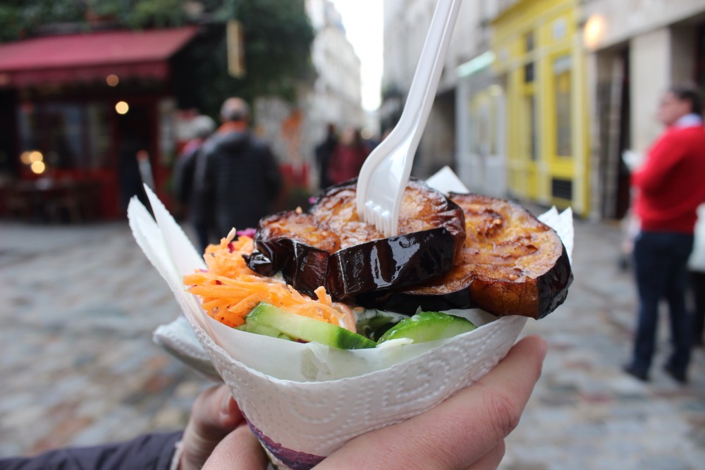Egg plant and falafel wrap with a cobblestone street and shops in the background in Le Marais in Paris, France