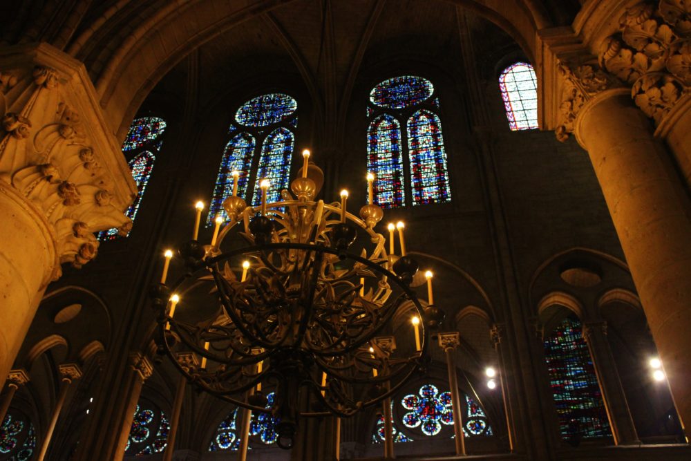 Inside Notre Dame in Paris with stained glass windows, pillars, and chandelier 