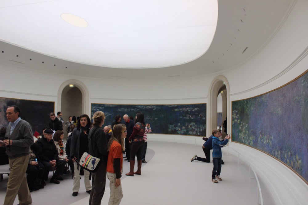 Water lily paintings in the Musee de l'Orangerie in a white oval room with people crowded in the center