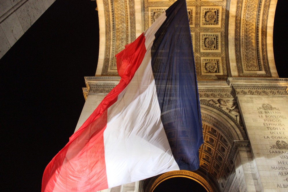 Arc de Triomphe at night with a light shining on a fluttering French Flag in Paris
