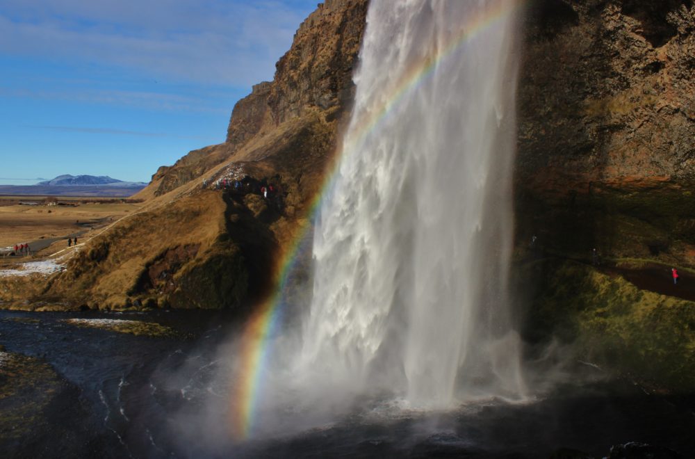 Side view of Seljalandsfoss with rainbow and blue skies, Iceland's South Coast